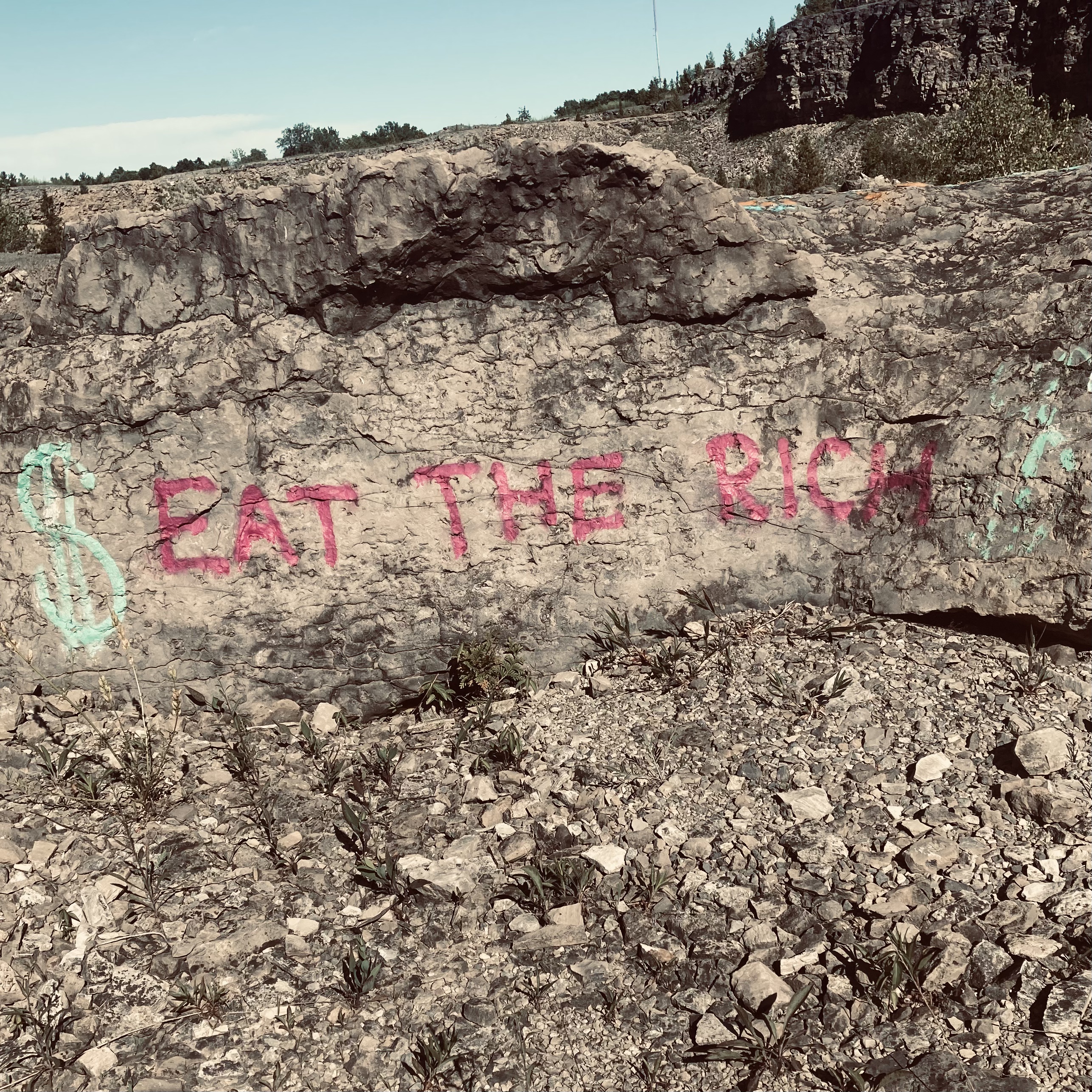 Photo of rock face with "eat the rich" in red spray paint.