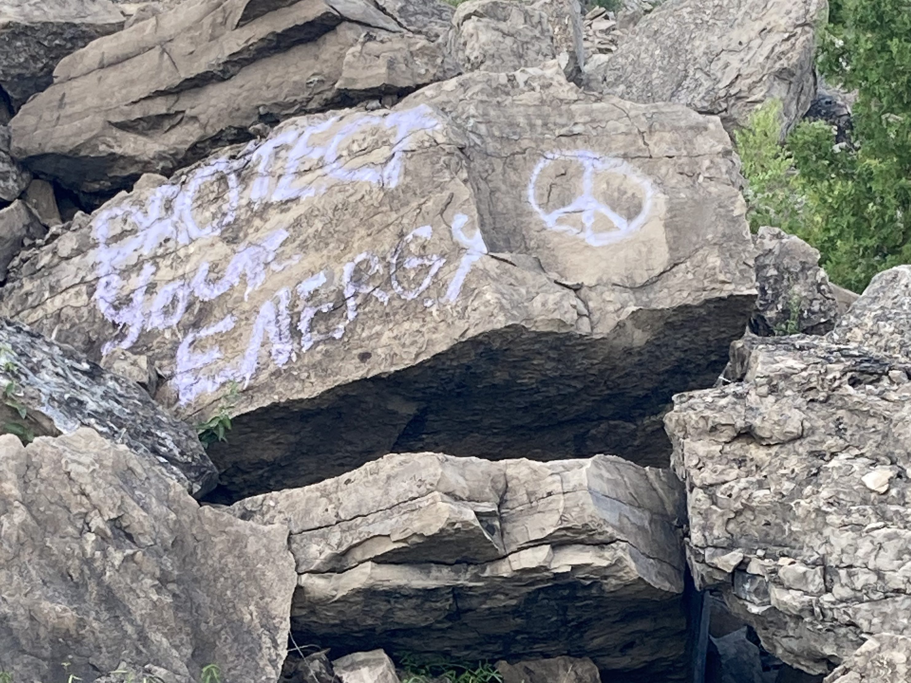 A pile of boulders, one with "Protect your energy" and a peace sign spray painted onto it
